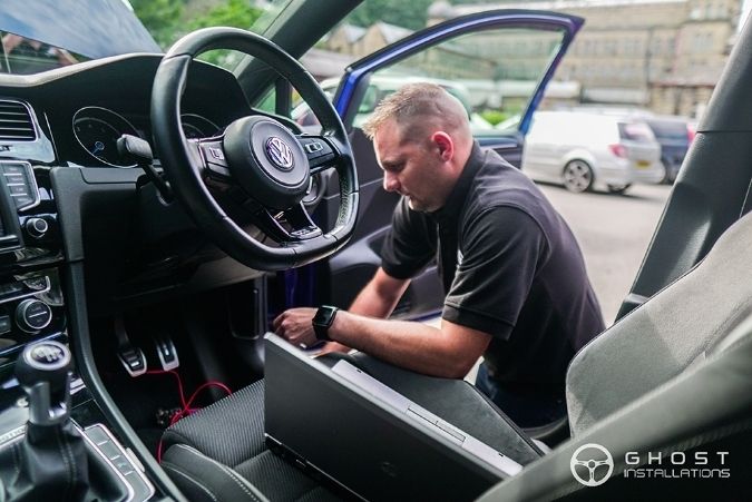 Ghost Installations engineer working on a laptop at the open driver's door of a car